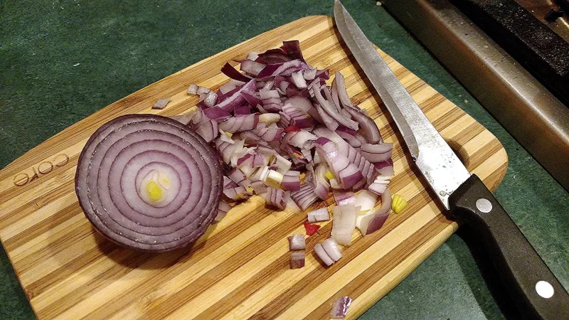 سكينة مطبخ جنب بصل أحمر متقطّع على لوح تقطيع خشب