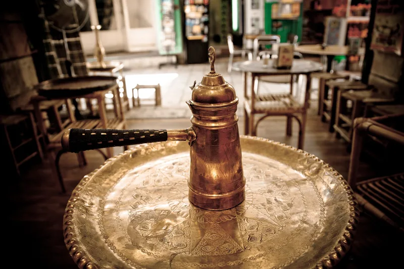 كنكة قهوة نحاس بإيد طويلة على صينية نحاس في قهوة صغيرة